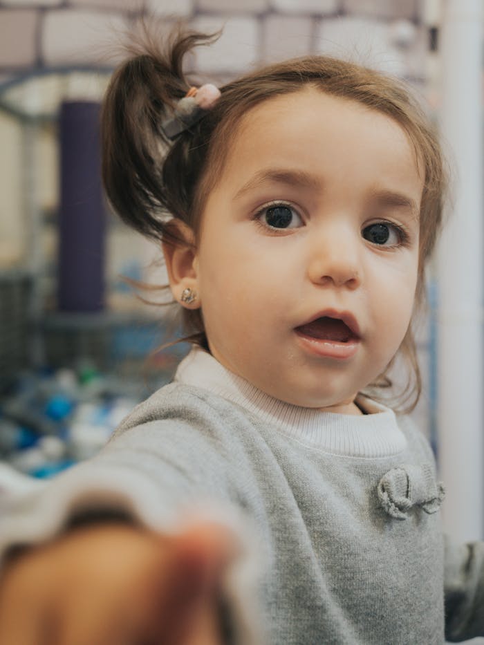 Cute toddler in a cozy sweater reaching towards camera with a playful expression indoors.