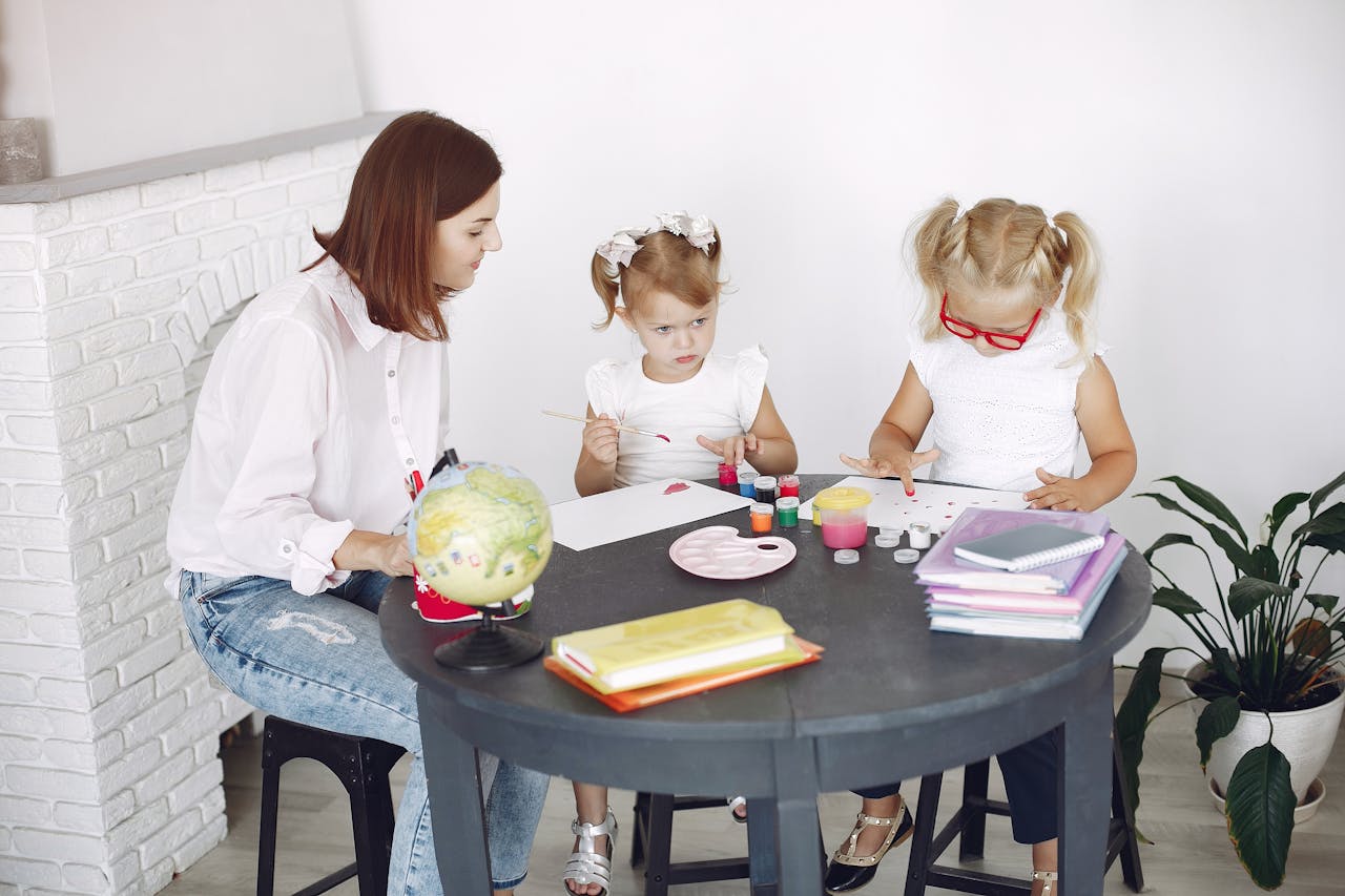 Small kids attentively painting in kindergarten with adult assistance while sitting together at round table