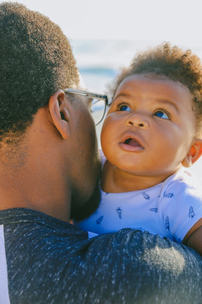 A loving father holds his baby close while enjoying a sunny day outdoors.