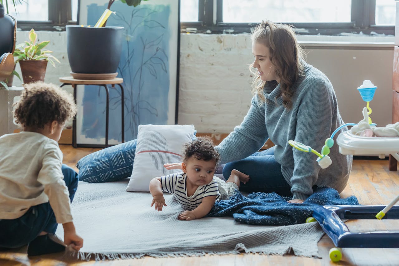 Positive mother playing with ethnic kids while sitting on floor in light living room